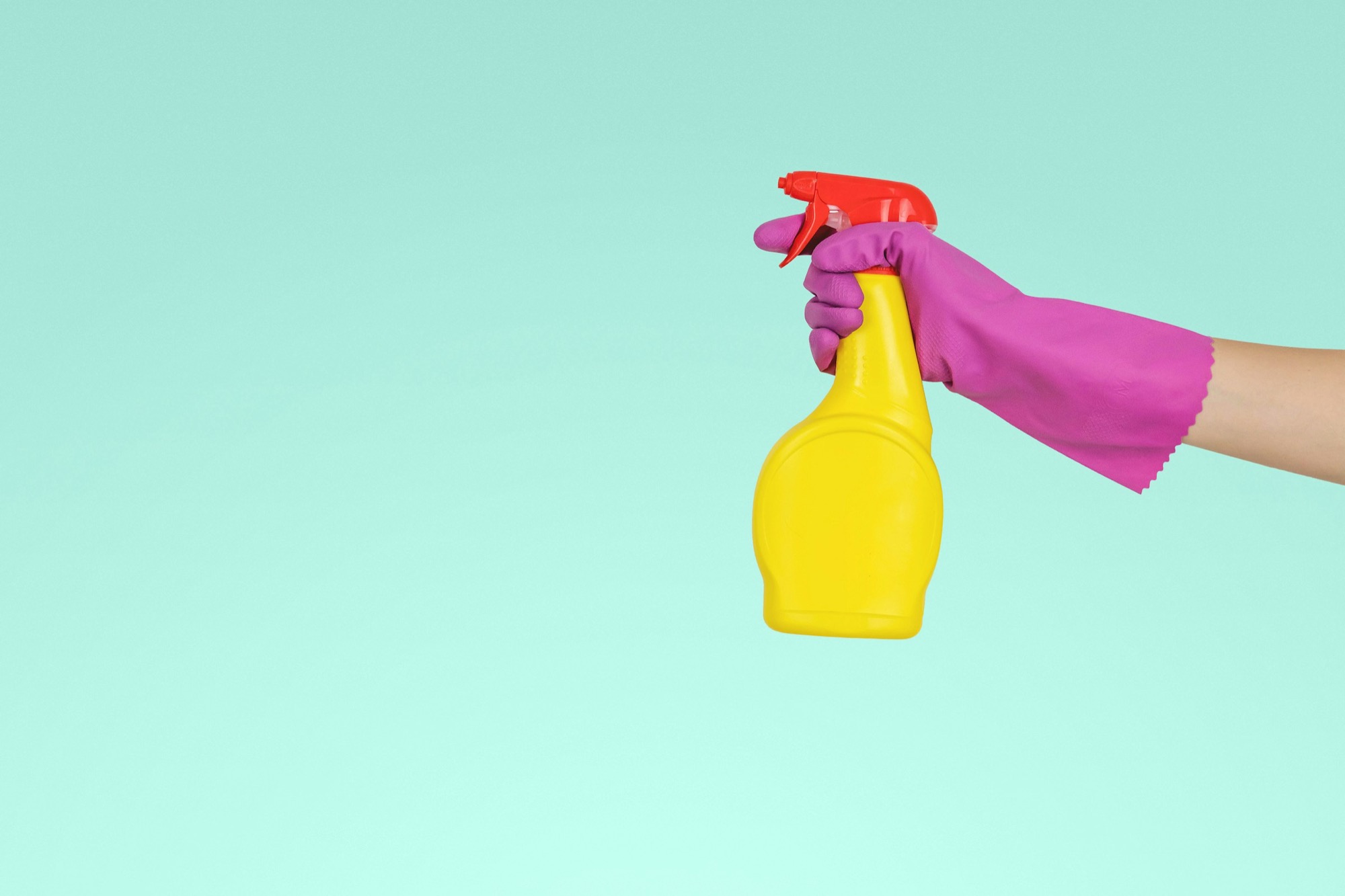 Mano con guanto che tiene un flacone spray su sfondo turchese
